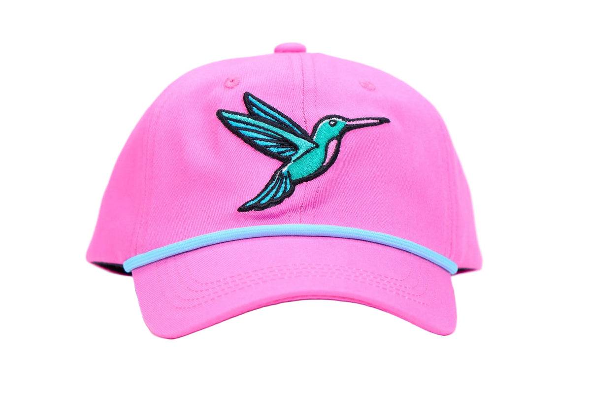 A bright pink baseball cap featuring an embroidered teal and black hummingbird on the front and a light blue stripe along the edge of the curved brim, set against a plain white studio background.