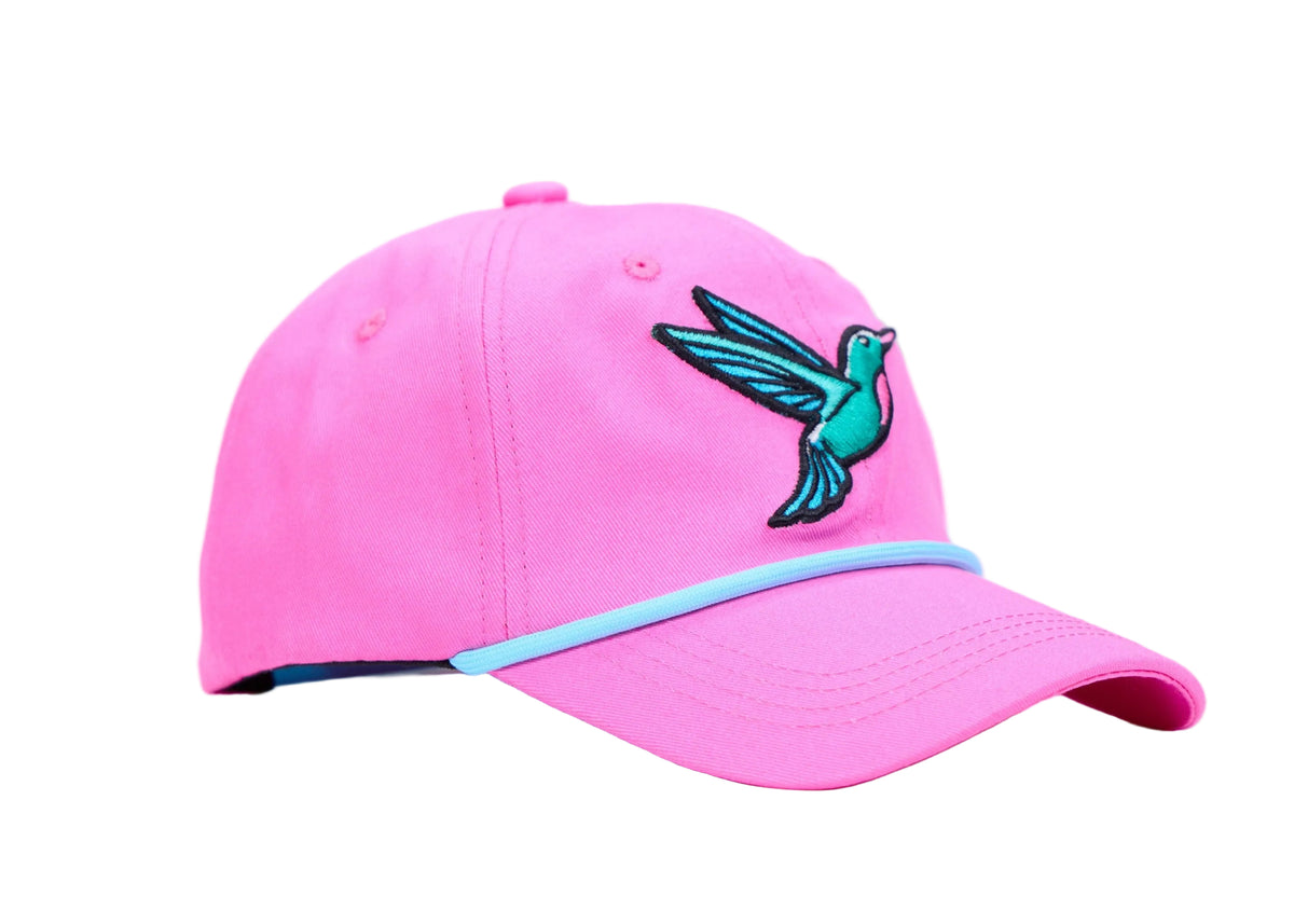A bright pink baseball cap featuring a turquoise and black embroidered hummingbird on the front and a light blue curved stripe across the visor, set against a plain white studio background.