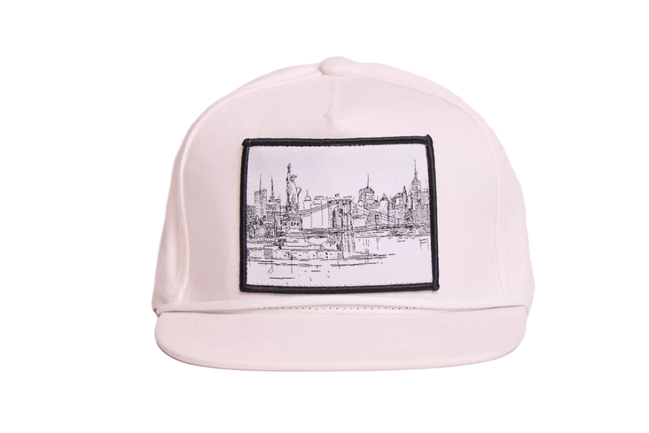 White flat bill hat featuring a patch with a line drawing of the New York City skyline