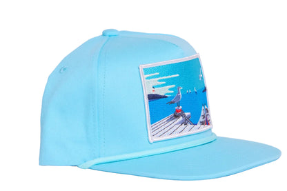 Aqua blue flat bill hat with a patch on the front featuring an ocean pier with a seagull and a boat