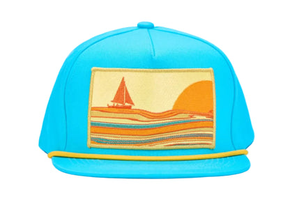 A bright turquoise blue snapback cap featuring a rectangular embroidered patch on the front with a sailboat and sunset scene in orange, yellow, and blue, set against a plain white background.