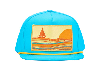 A bright turquoise blue snapback cap featuring a rectangular embroidered patch on the front with a sailboat and sunset scene in orange, yellow, and blue, set against a plain white background.