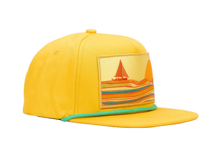 A bright yellow flat-brim cap with a rectangular embroidered patch on the front depicting a sailboat and striped waves. A thin mint green trim accents the edge of the brim, set against a plain white background.