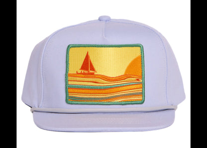 A light grey flat-brim cap featuring a square embroidered patch on the front with a sailboat scene in yellow, orange, and green.
