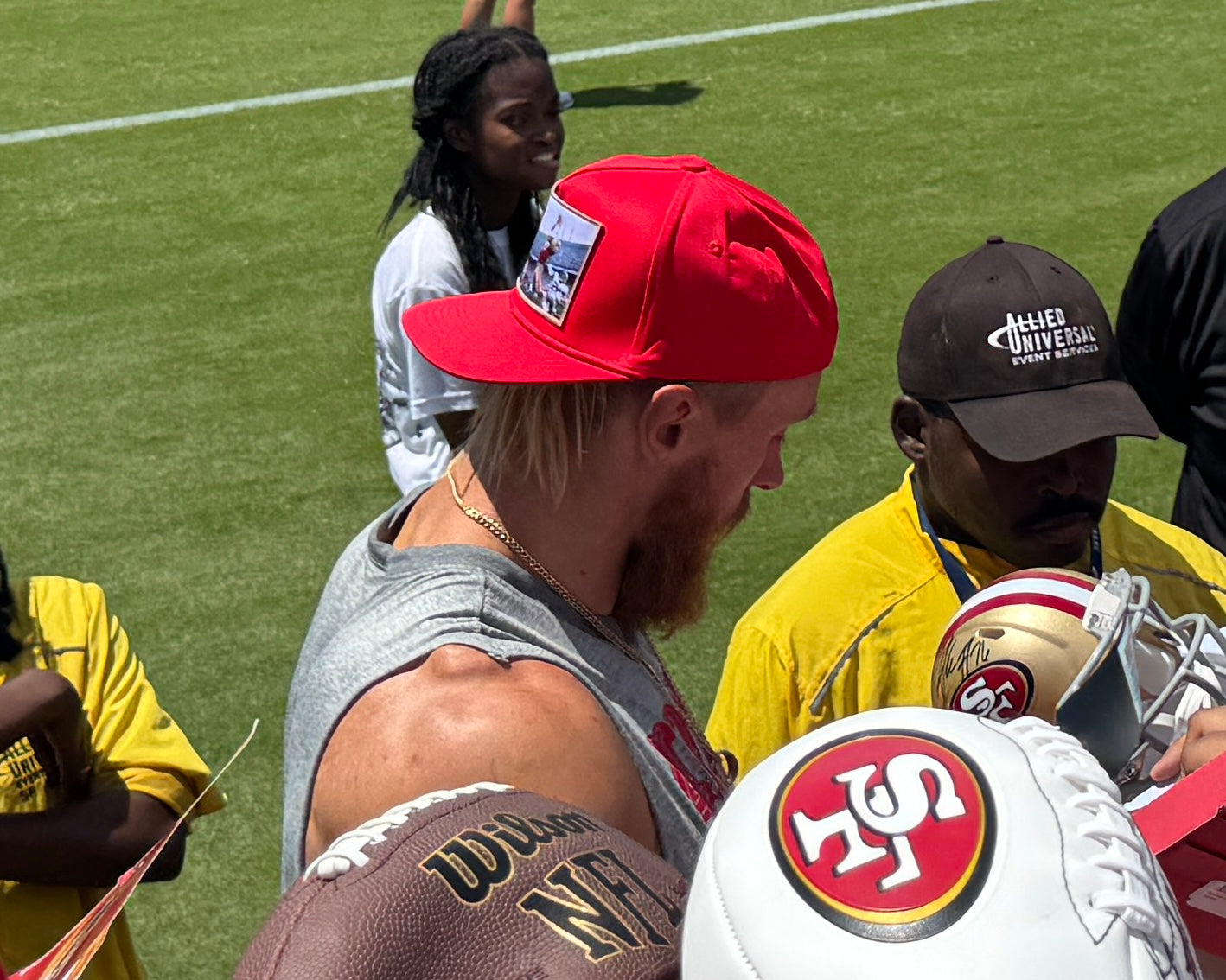 George Kittle of the 49ers wearing a red hat featuring a photographic patch with a gold border.  The image is of The Catch, the legendary touchdown caught by Dwight Clark of the 49ers