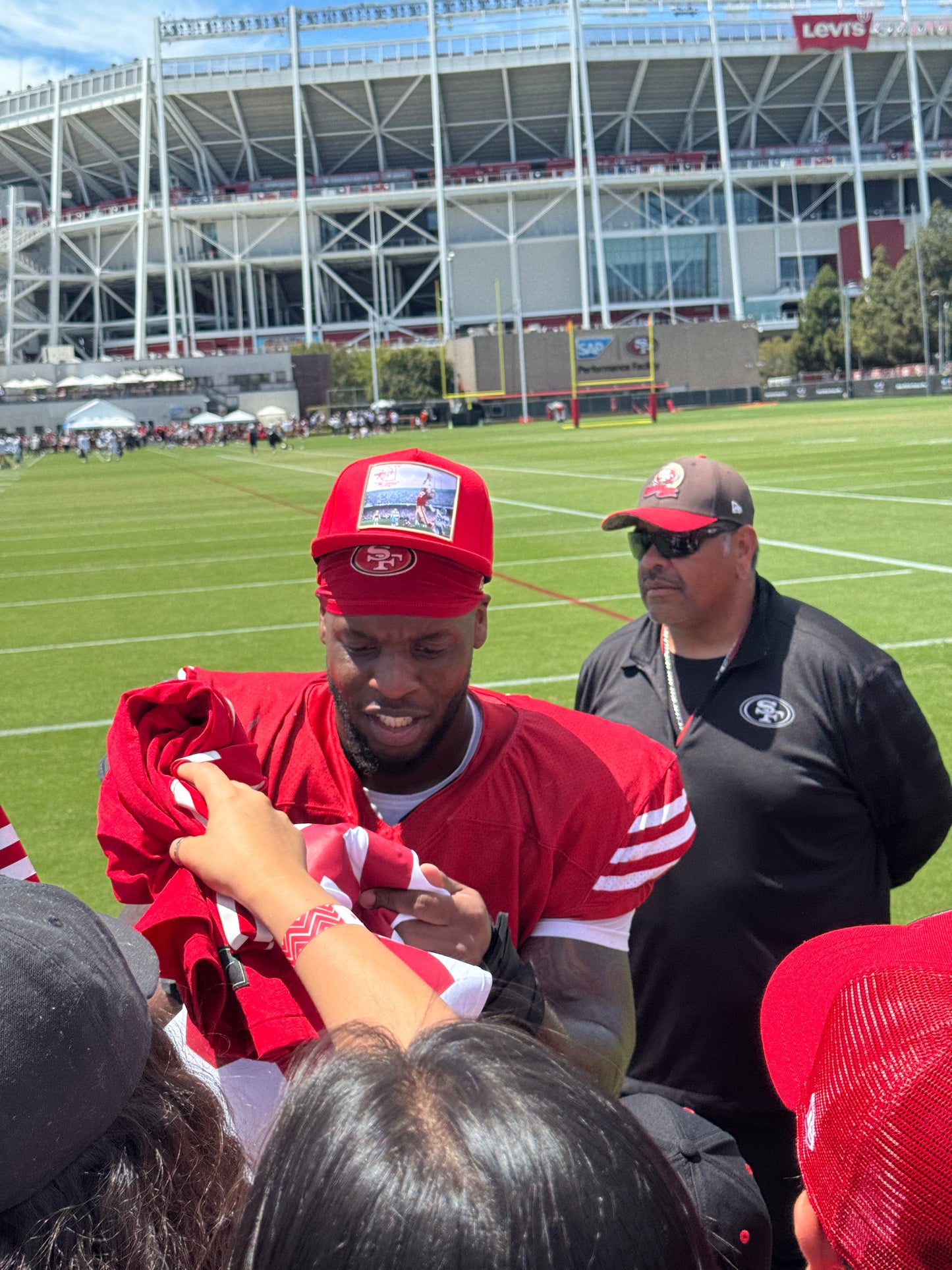 A training camp player wearing a red hat featuring a photographic patch with a gold border.  The image is of The Catch, the legendary touchdown caught by Dwight Clark of the 49ers